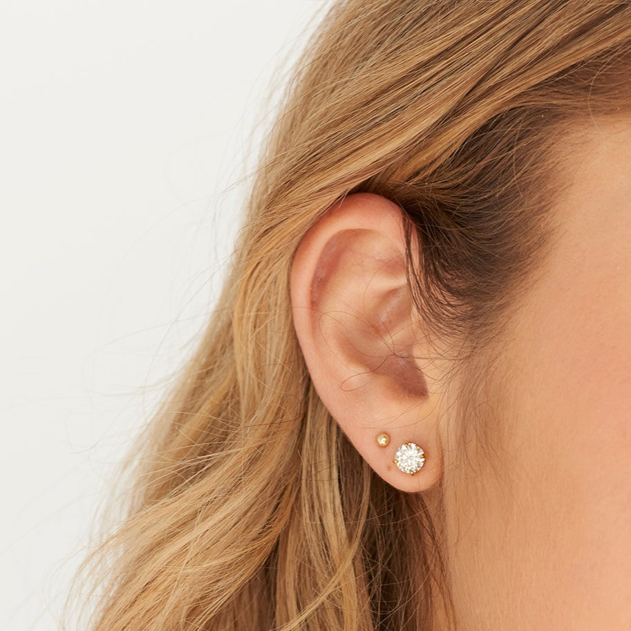 Close-up of a woman wearing moisssanite stud earrings with a plain background