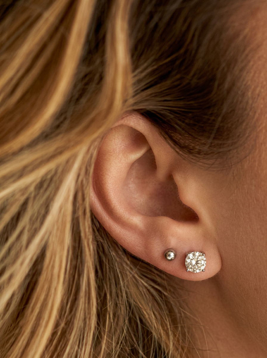 Close-up of an ear wearing  diamond stud earrings with blonde hair.